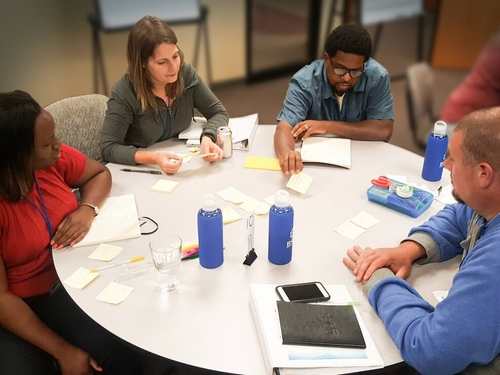 Teacher talking to students who are working around a table.