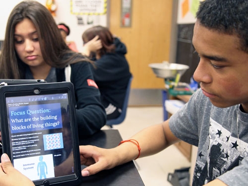 male student holding an iPad that says "Focus Question: What are the building blocks of living things?"