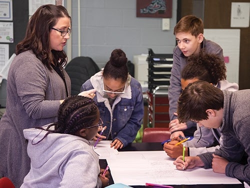 Teacher talking to students who are working around a table.