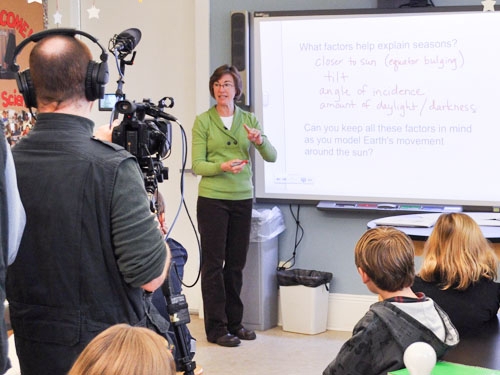 Female teacher in front of class of students and man with video camera