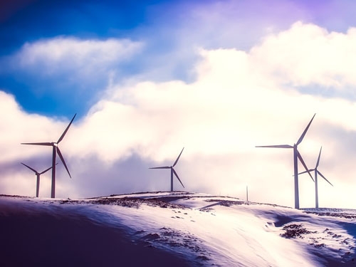 Five white windmills on a snowy hill with a blue sky and white clouds.